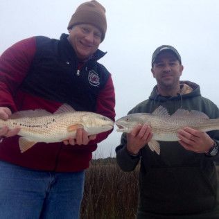 Two people holding large fish outdoors on a cloudy day