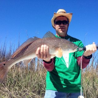 Angler in cowboy hat holding a large fish outdoors against a blue sky
