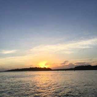Sunset over calm water with a glowing horizon and silhouetted shoreline