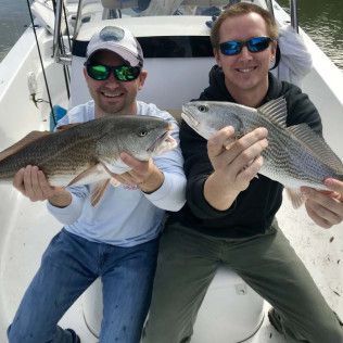 Two anglers on a boat holding large fish and smiling at the camera
