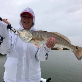 Person in a white jacket holds a large fish on a boat over calm water.