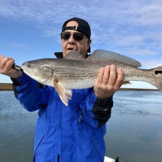 Angler in blue jacket holding a large fish at the beach under a blue sky