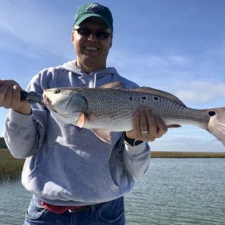 Person holding a large fish on a boat, smiling under a blue sky on the water.