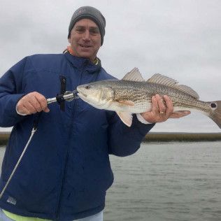 Man in blue jacket holding a large fish on a boat under a cloudy sky