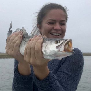 Smiling woman holding a large silver fish by the water