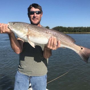 Man holding a large fish on a boat in calm water under a clear sky