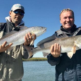 Two anglers holding large fish on a boat under a clear blue sky.