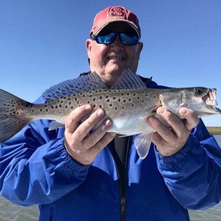 Person in blue jacket holding a speckled fish against a clear blue sky