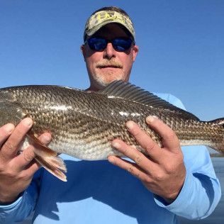 Man holding a large fish outdoors against a blue sky, wearing a cap and sunglasses