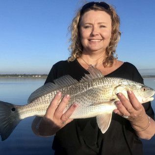 Woman holding a large silver fish by the water at sunset