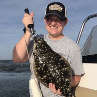 Smiling person on a boat holding a large spotted fish by the tail