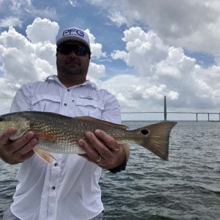 Person holding a large fish on a boat with choppy water and a bridge in the background