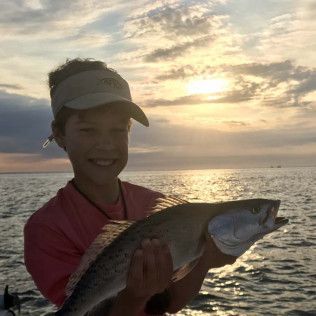 Person holding a fish at sunset by the water