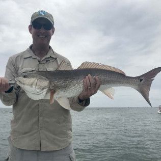 Man holding a large striped fish on a boat with gray water and cloudy sky in the background