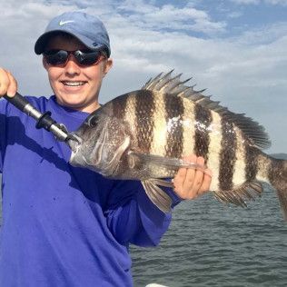 Person holding a large striped fish on a boat, wearing a blue shirt and cap, smiling on the water