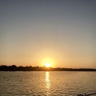Sunset over calm water with a bright reflection and silhouetted shoreline