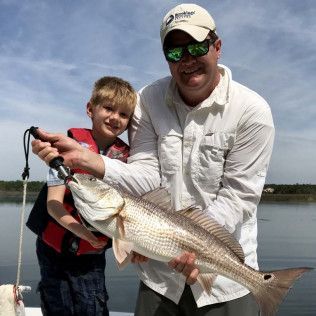 Man and boy holding a large striped fish by a calm lakeshore