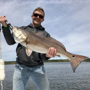 Smiling angler holding a large striped fish on a boat with open water behind him