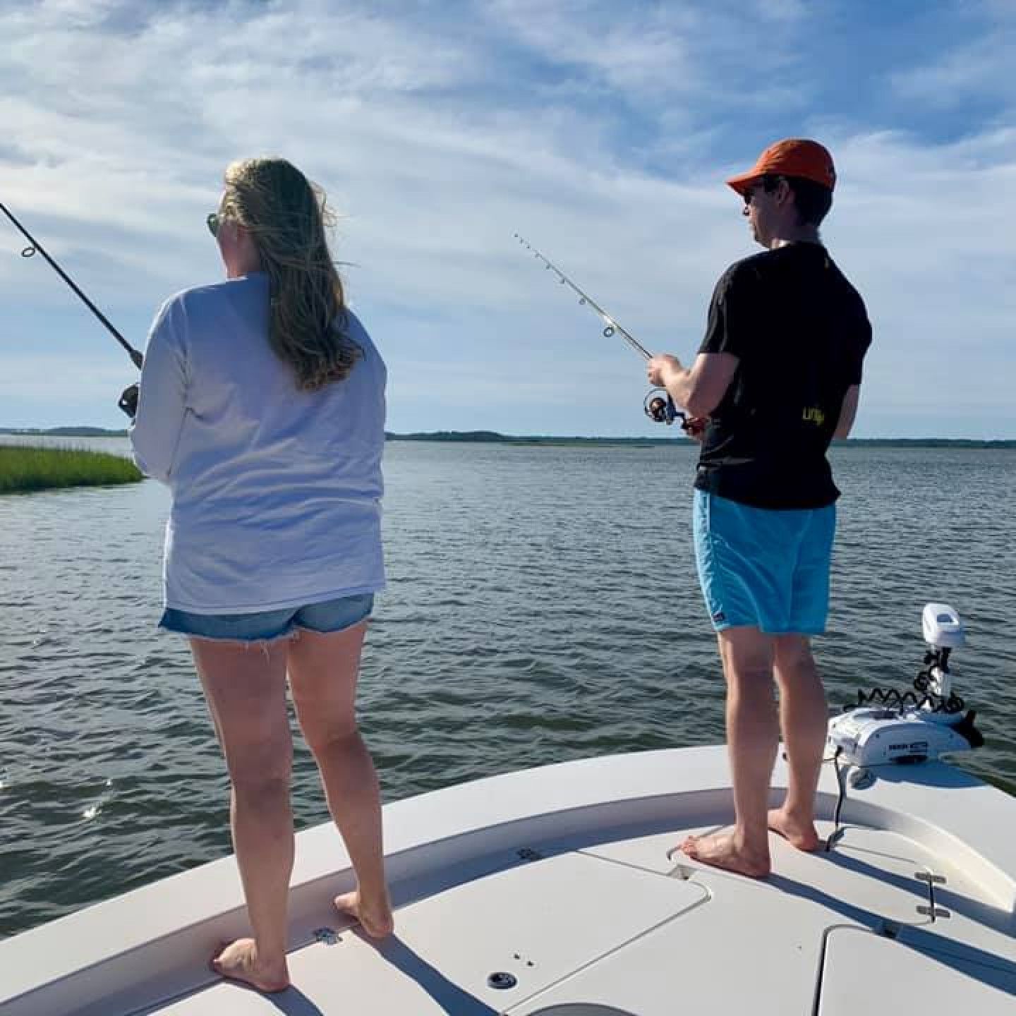 Two people fishing from a boat on calm water under a partly cloudy sky