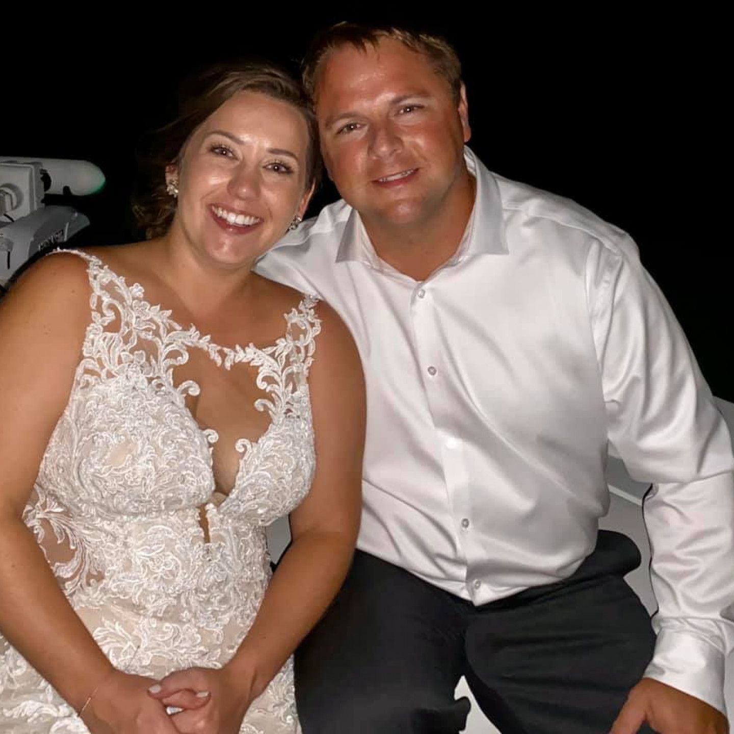 Smiling couple in white attire seated together at a nighttime event