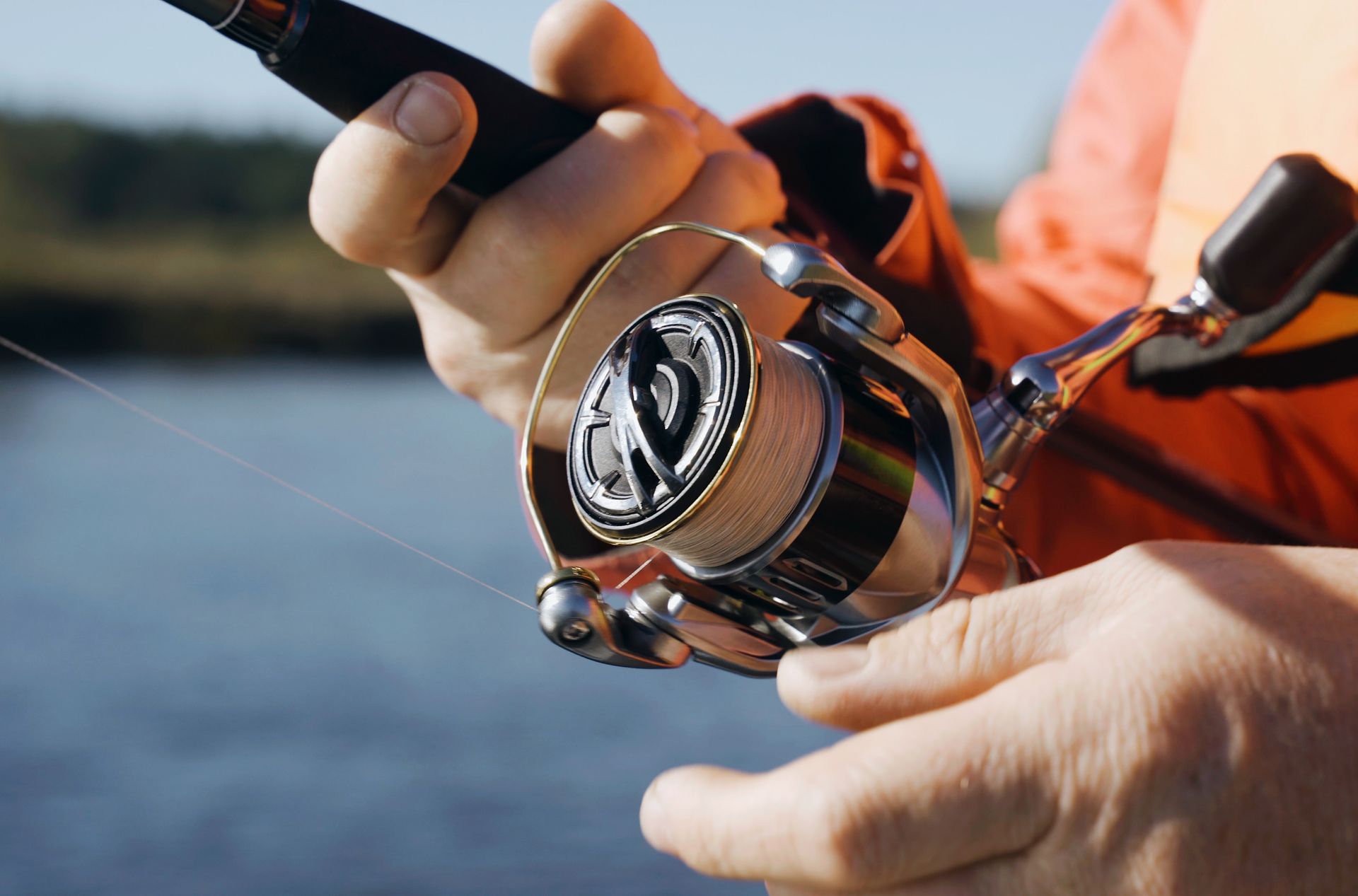 Close-up of hands holding a fishing rod and reel by the water
