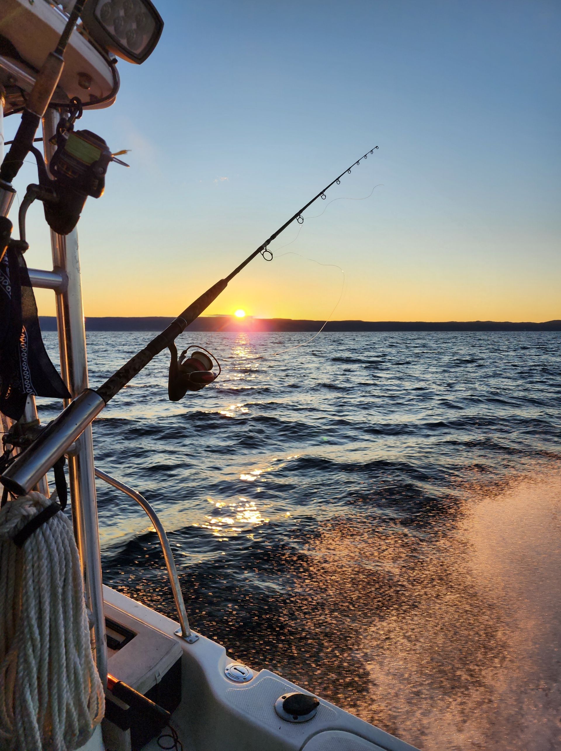 Fishing rod on a boat at sunset, with waves splashing and the sun near the horizon.