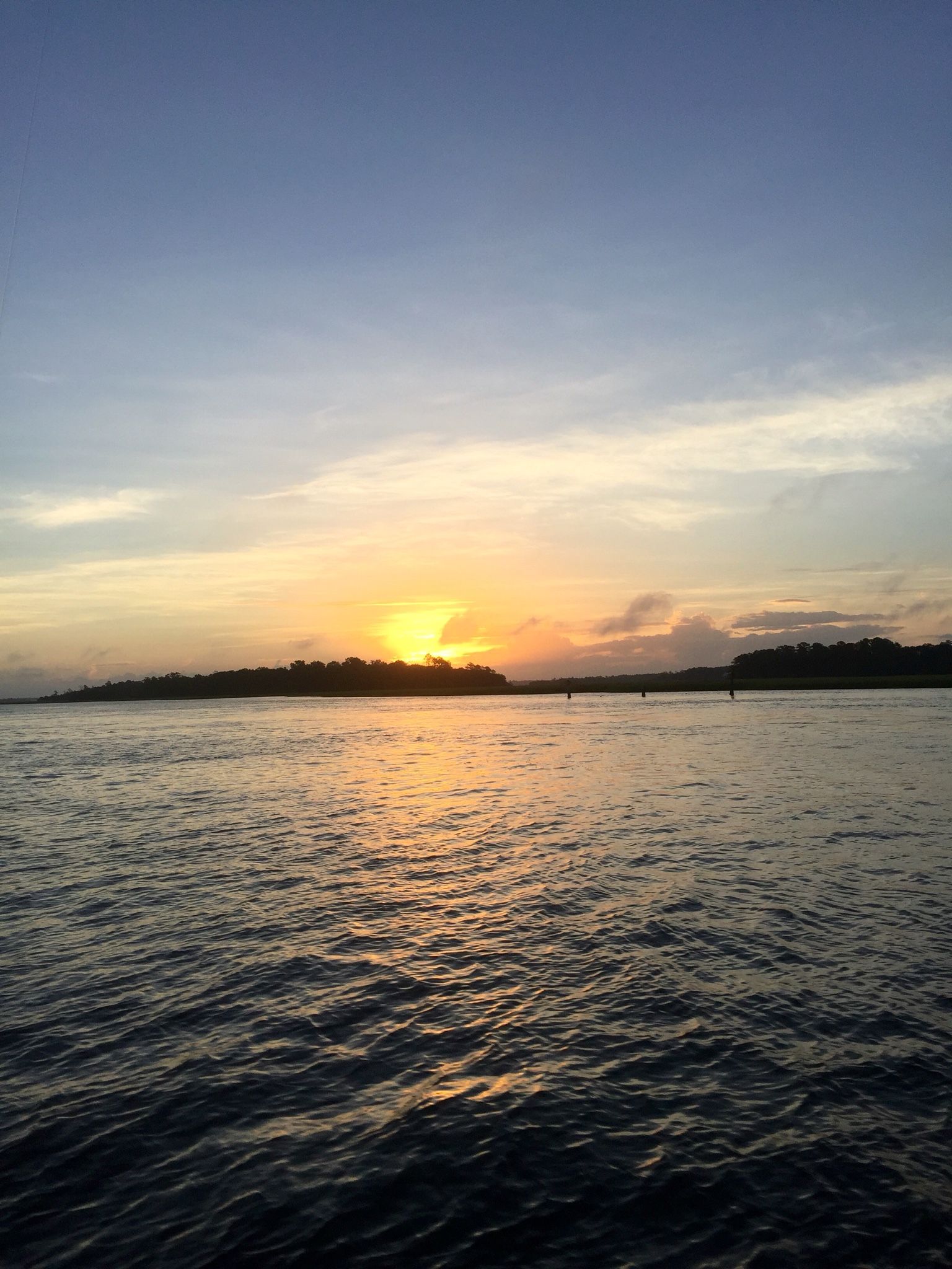 Sunset over calm water with a glowing orange horizon and dark shoreline silhouettes