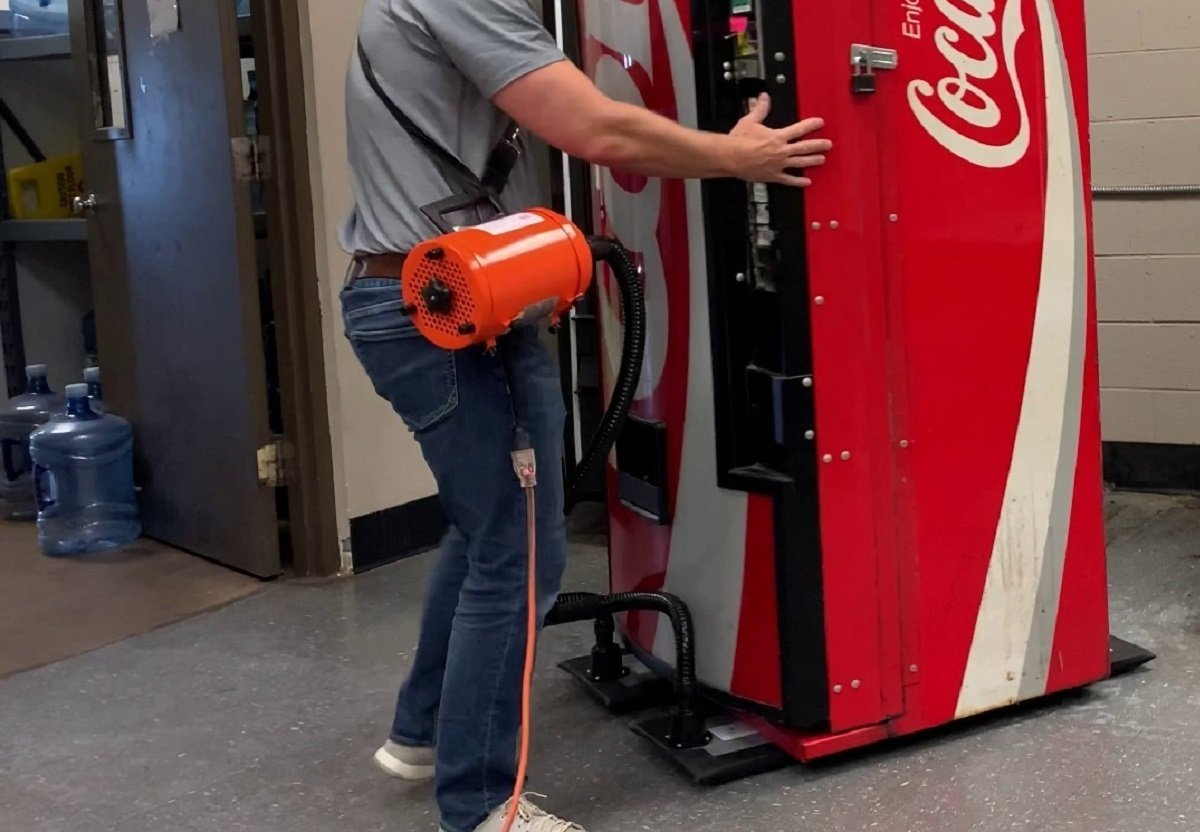 En person bruker en oransje luftdrevet Airsled luftløfter til å skyve en rød Coca-Cola-automat over et flislagt gulv.