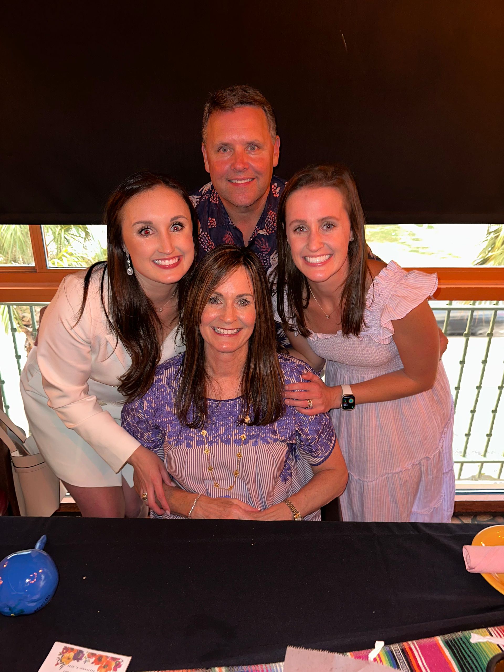 Four people posing together at a table, smiling at the camera in a dimly lit indoor setting.