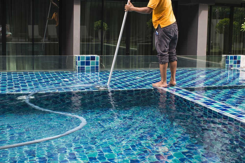 A Person Using a Long-handled Tool to Clean a Blue-tiled Swimming Pool — Cascade Pool & Spa Centre in Laurieton, NSW