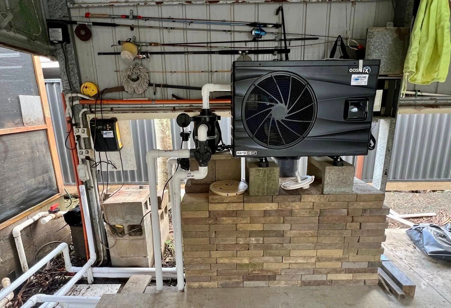 A Dark, Square Pool Heat Pump Installed on a Brick Base, With Pipes and Control Boxes — Cascade Pool & Spa Centre in Kempsey, NSW