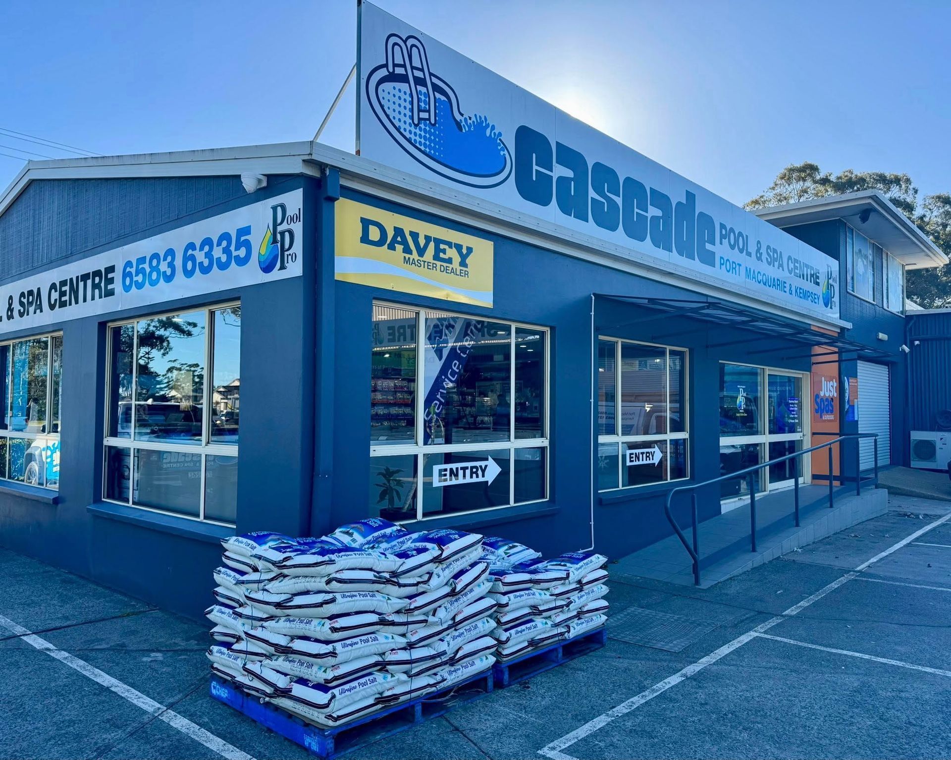 A Cascade Pool & Spa Centre Store With Blue Exterior, Davey Equipment Sign, and Stacked Bags of Product Outside — Cascade Pool & Spa Centre in Port Macquarie, NSW