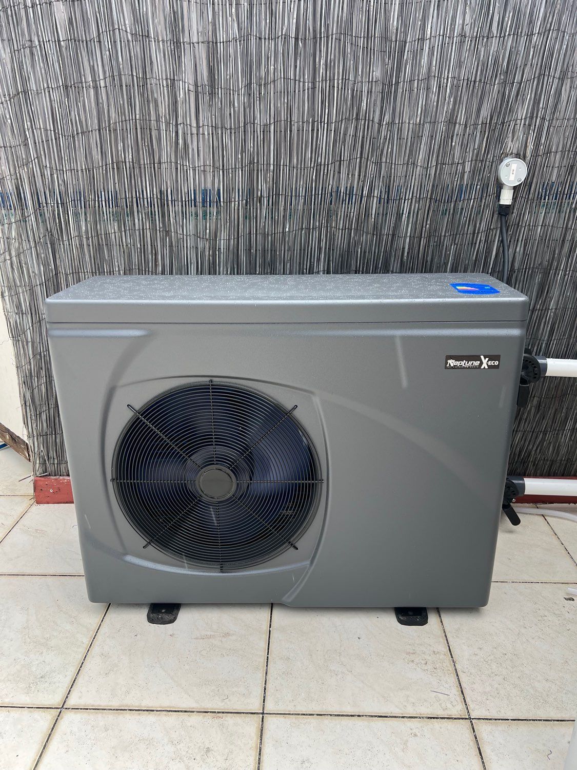 Gray outdoor air-conditioning unit with large fan on a tiled patio against a textured wall. — Cascade Pool & Spa Centre in Port Macquarie, NSW