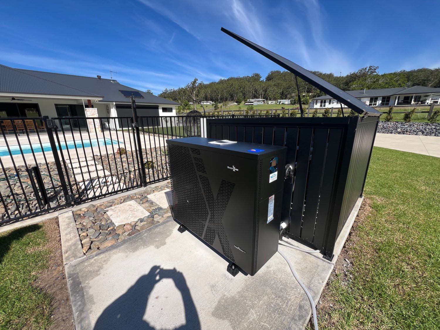 Black utility cabinet beside a pool fence and grassy lawn on a sunny day
