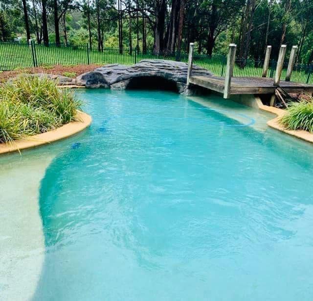 Turquoise swimming pool with a small stone bridge and lush greenery around it — Cascade Pool & Spa Centre in Port Macquarie, NSW