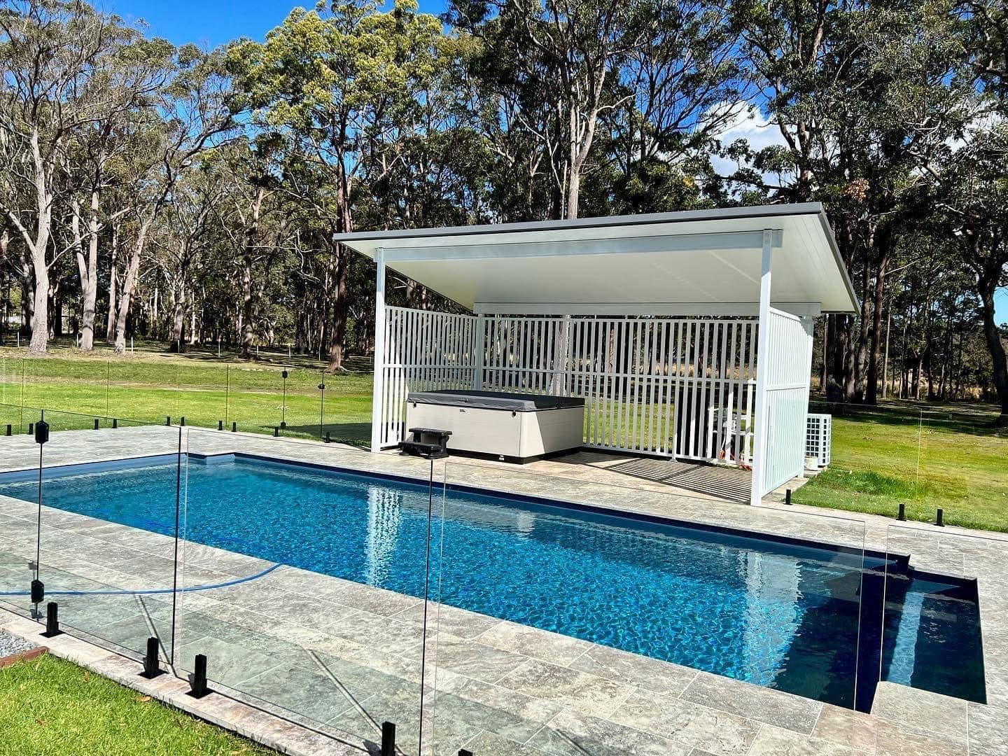 Modern backyard pool with blue water, white pergola cabana, and glass fencing amid trees— Cascade Pool & Spa Centre in Port Macquarie, NSW