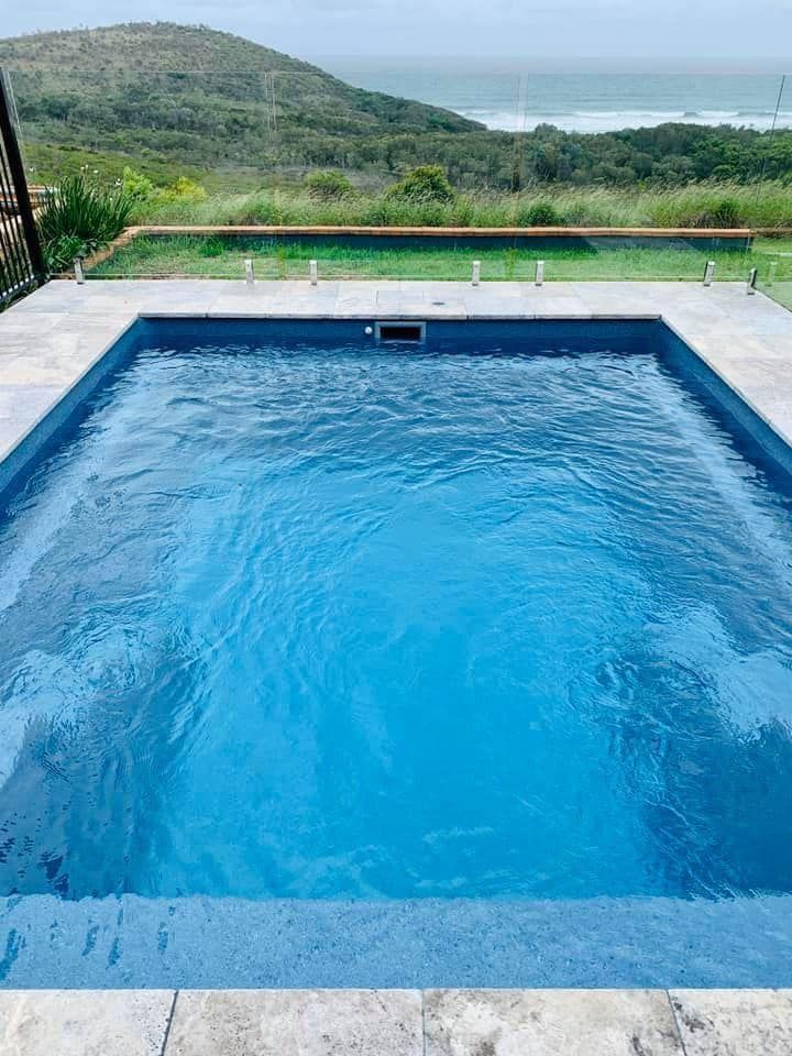 Blue infinity pool overlooking green hills and the ocean under a cloudy sky — Cascade Pool & Spa Centre in Port Macquarie, NSW