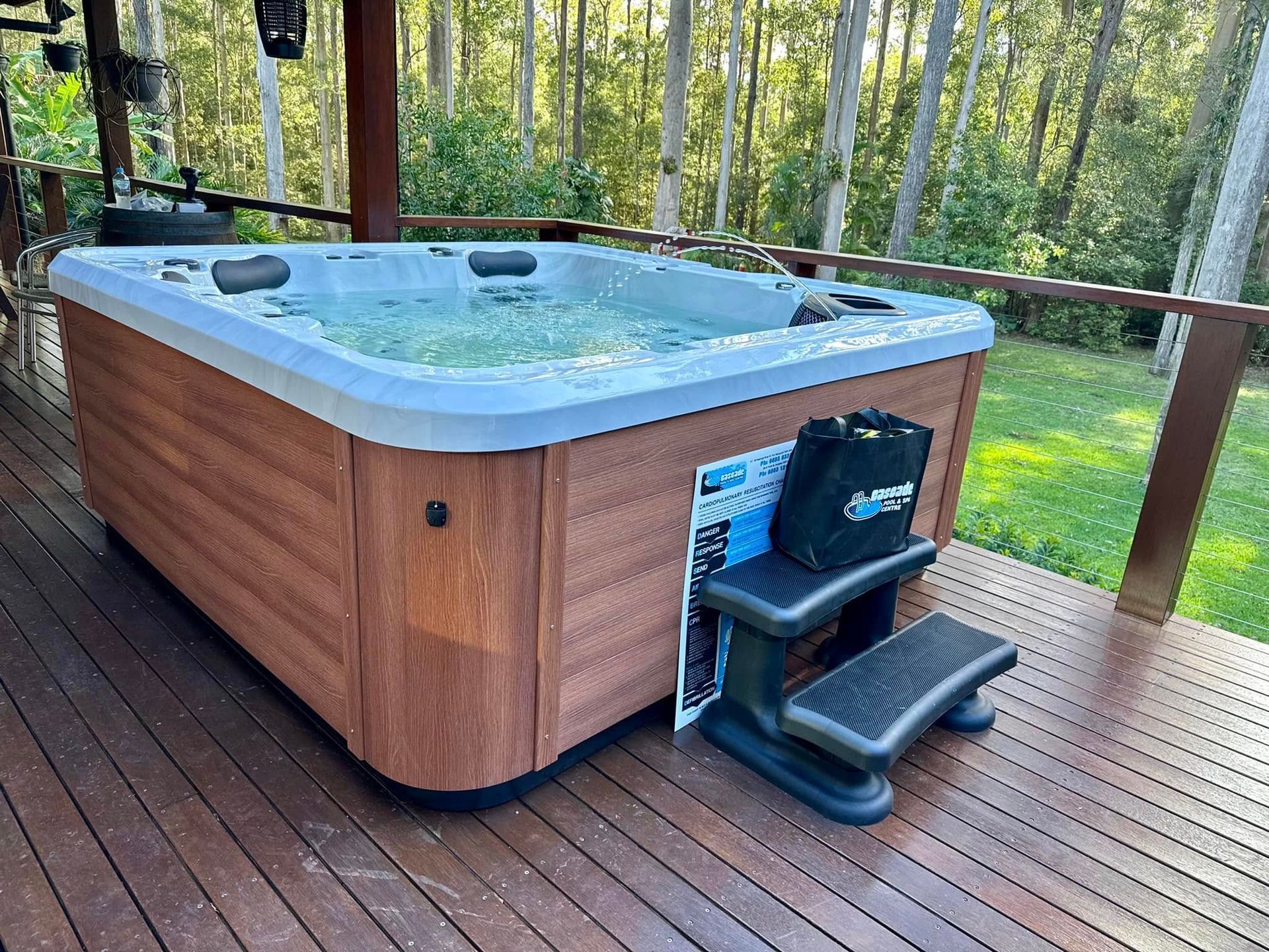 Wood-paneled hot tub on a wooden deck overlooking a forest, with steps and a cover lift attached. — Cascade Pool & Spa Centre in Port Macquarie, NSW