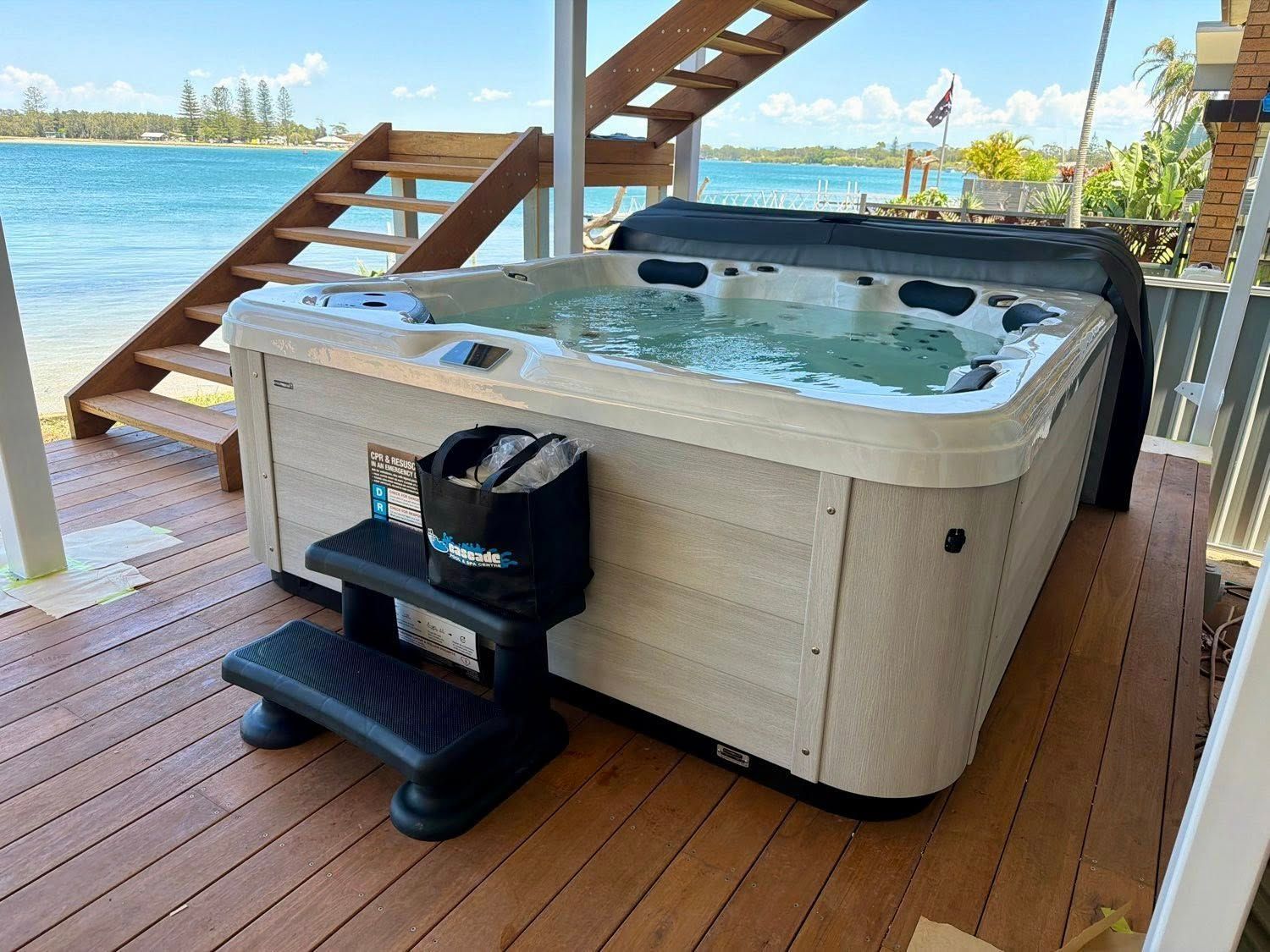 Hot tub on a wooden dock beside a lake, with stairs and a small table in front. — Cascade Pool & Spa Centre in Port Macquarie, NSW
