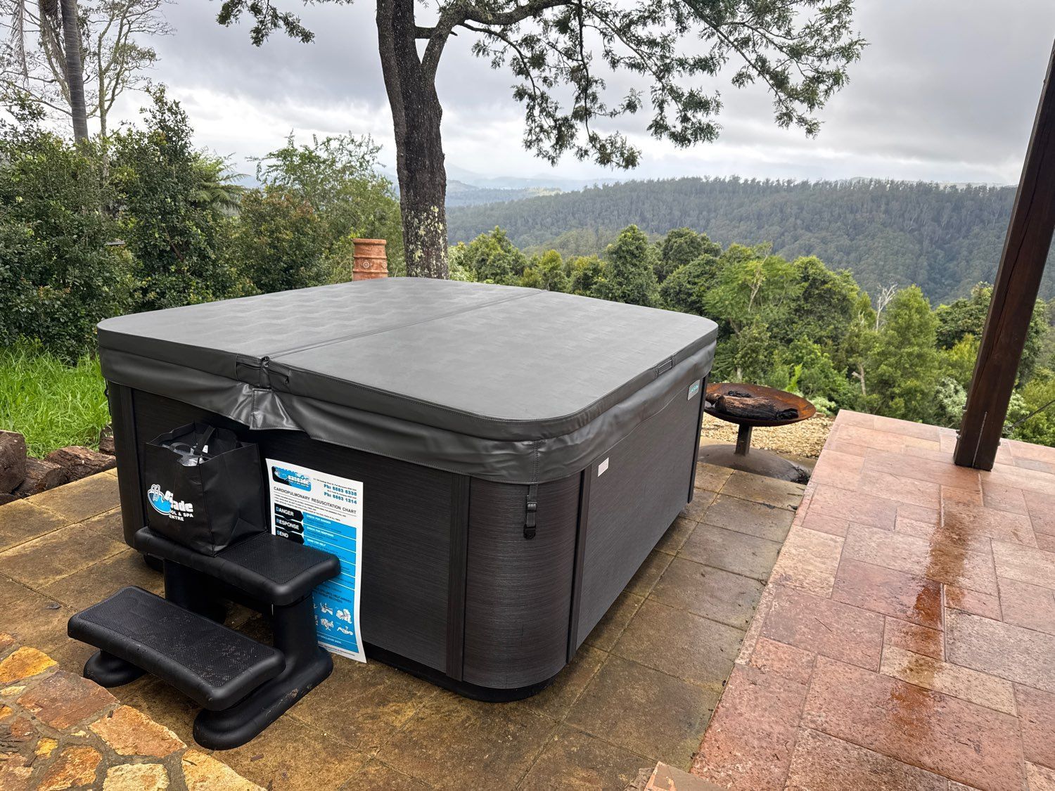 Black hot tub on a patio overlooking a misty wooded valley — Cascade Pool & Spa Centre in Port Macquarie, NSW