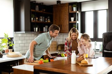 A family prepares a meal together in a modern kitchen, smiling as they work with fresh produce at a wooden island.