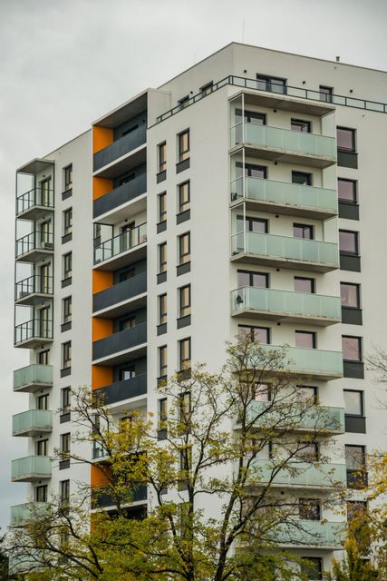 Modern white apartment building with orange balcony accents and trees in front