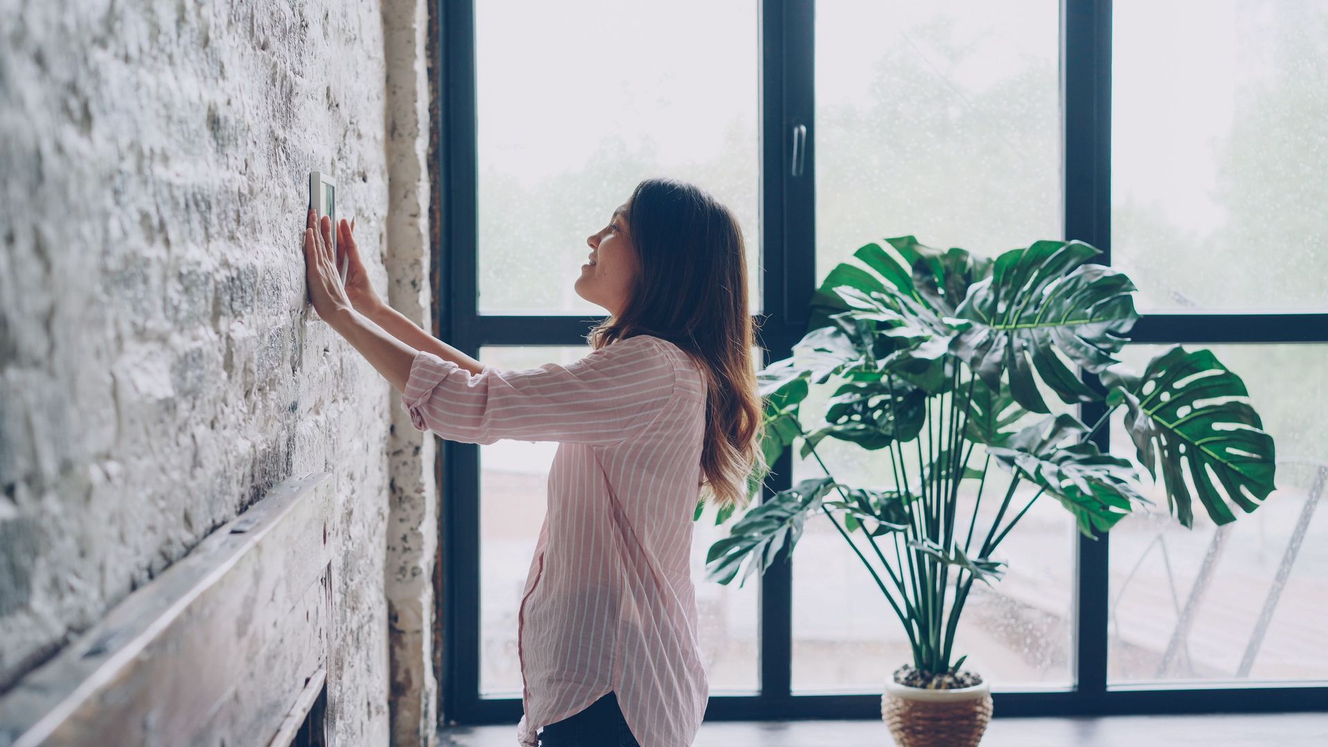 A resident adjusting curtains beside a sunlit window.