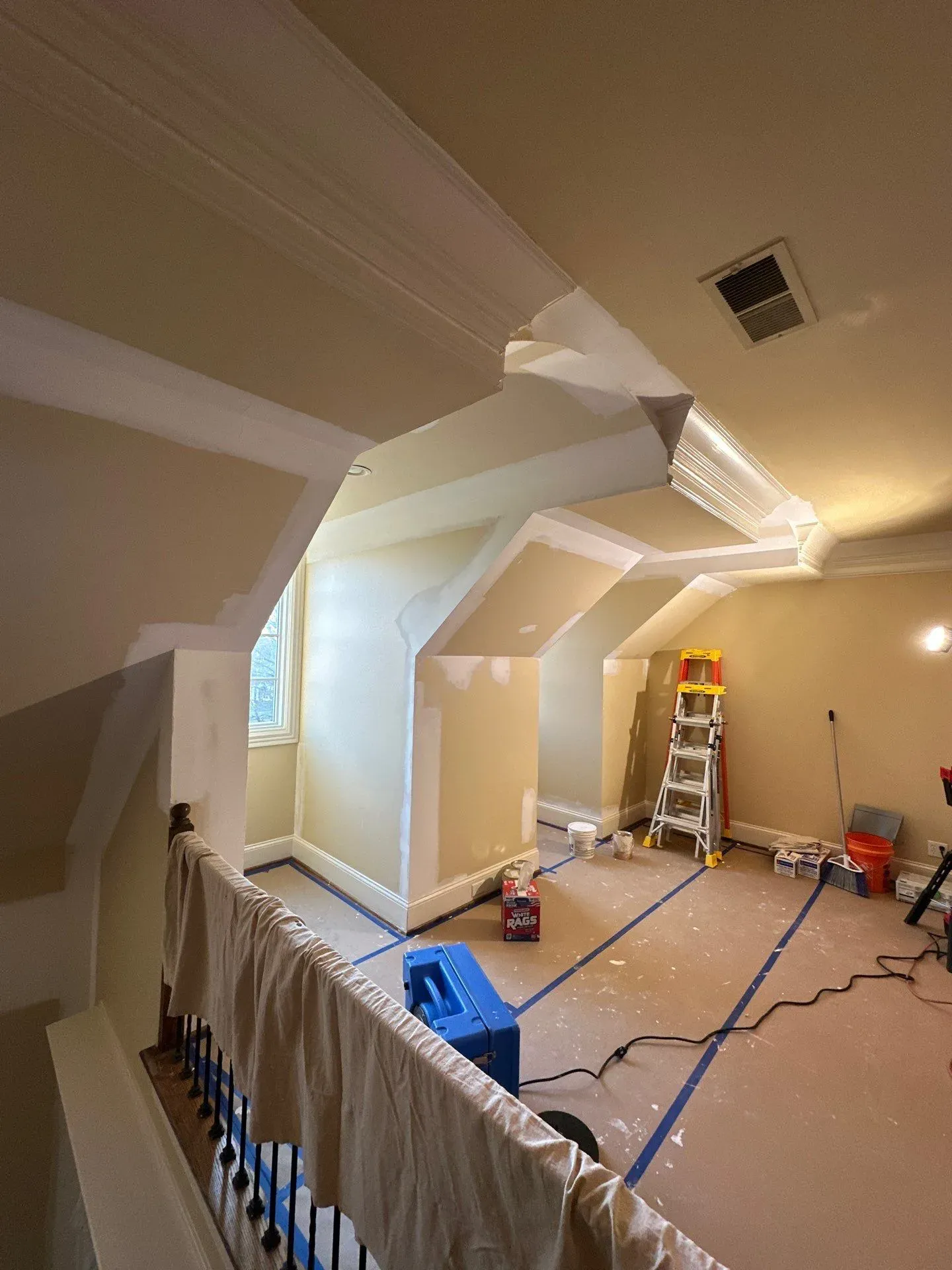 Interior room with angled ceilings, freshly painted walls, trim, and construction materials.