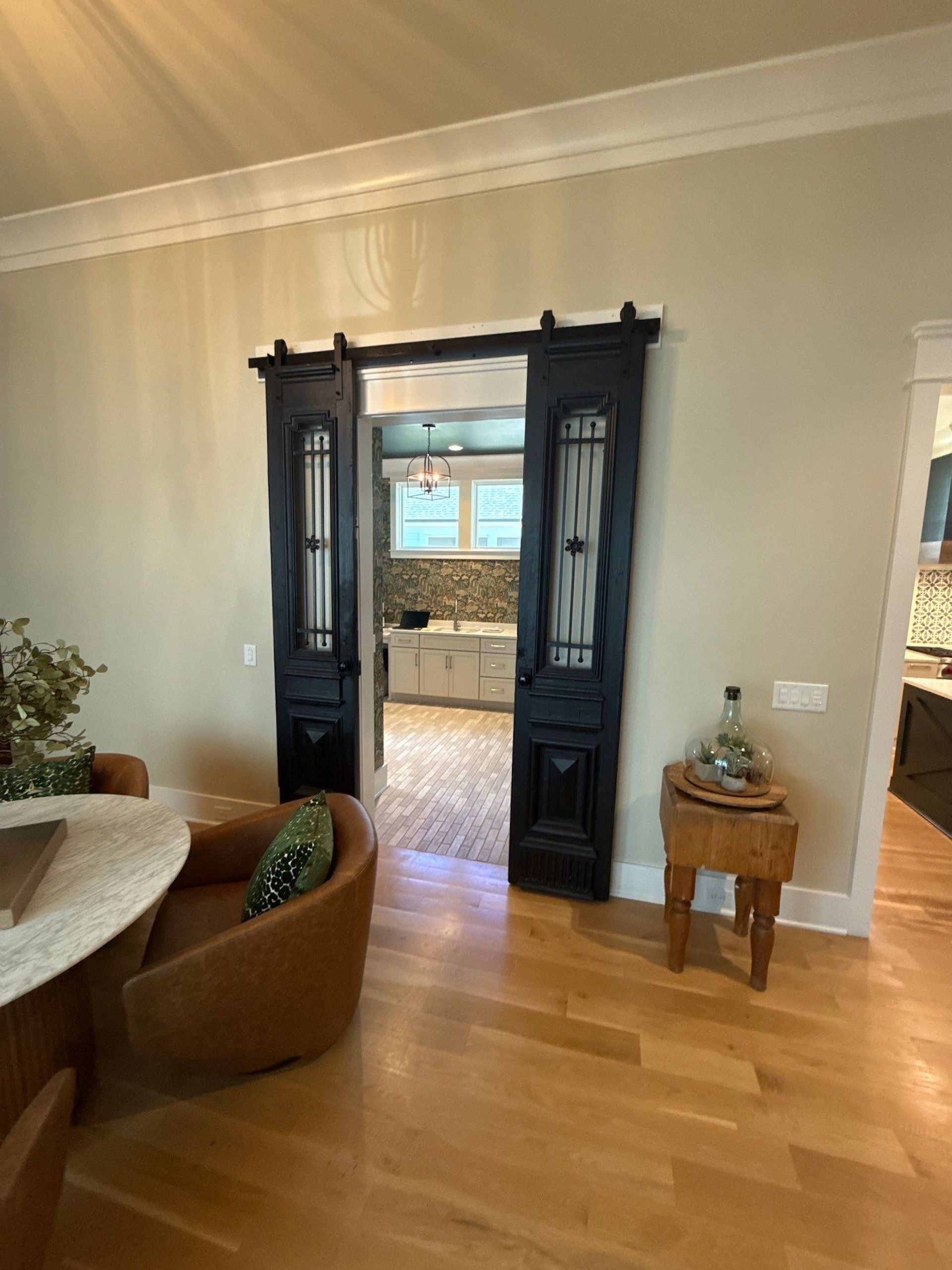 Black sliding doors open to a kitchen with white cabinets, light countertops, and wood flooring.