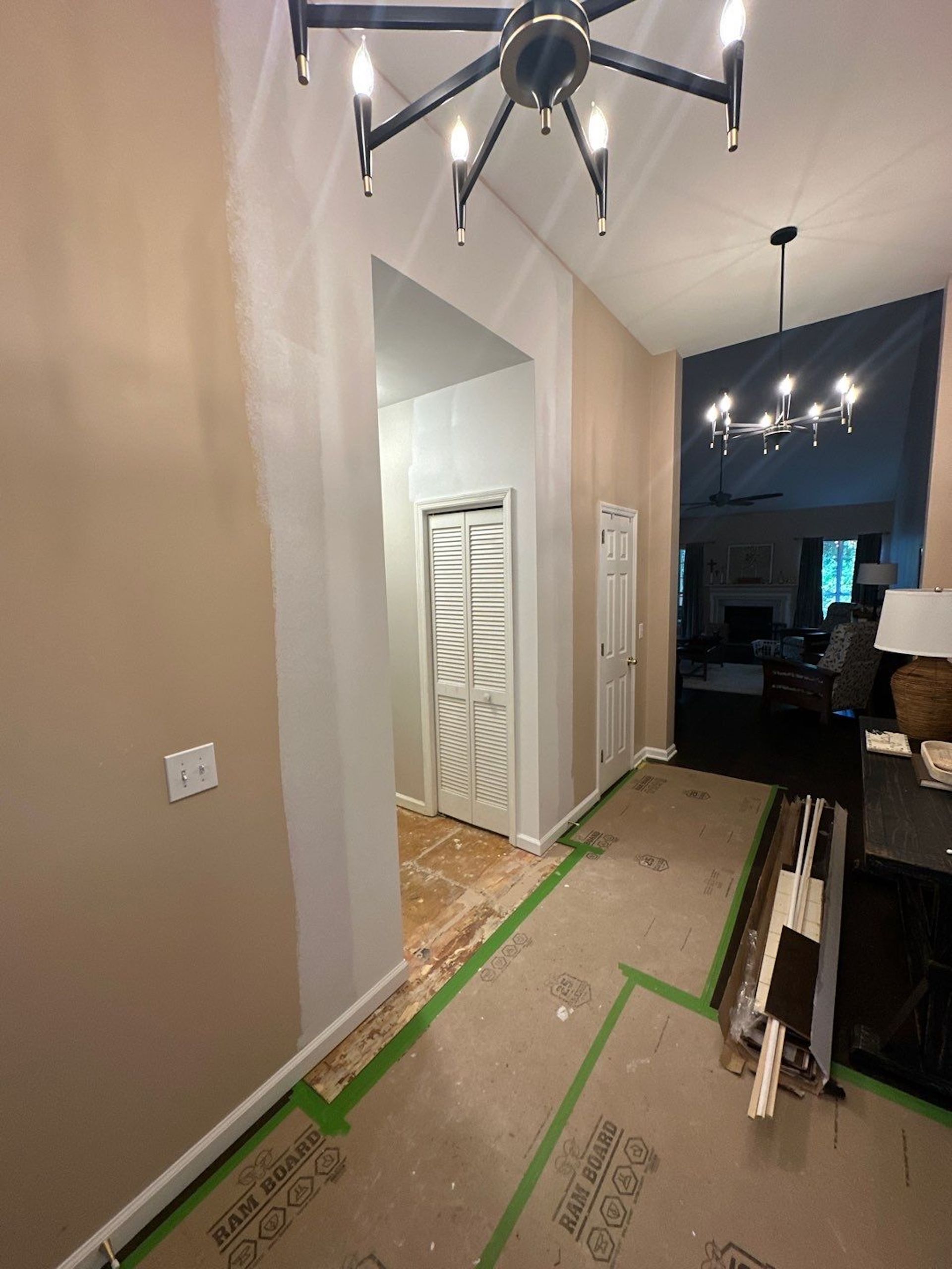 Hallway under renovation with tan walls, white trim, and two chandeliers.