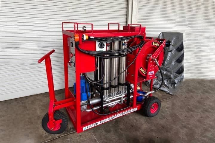 A red machine with wheels is sitting on a concrete floor.