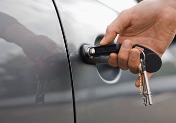 Hand inserting car key into gray car door lock with a keyring attached