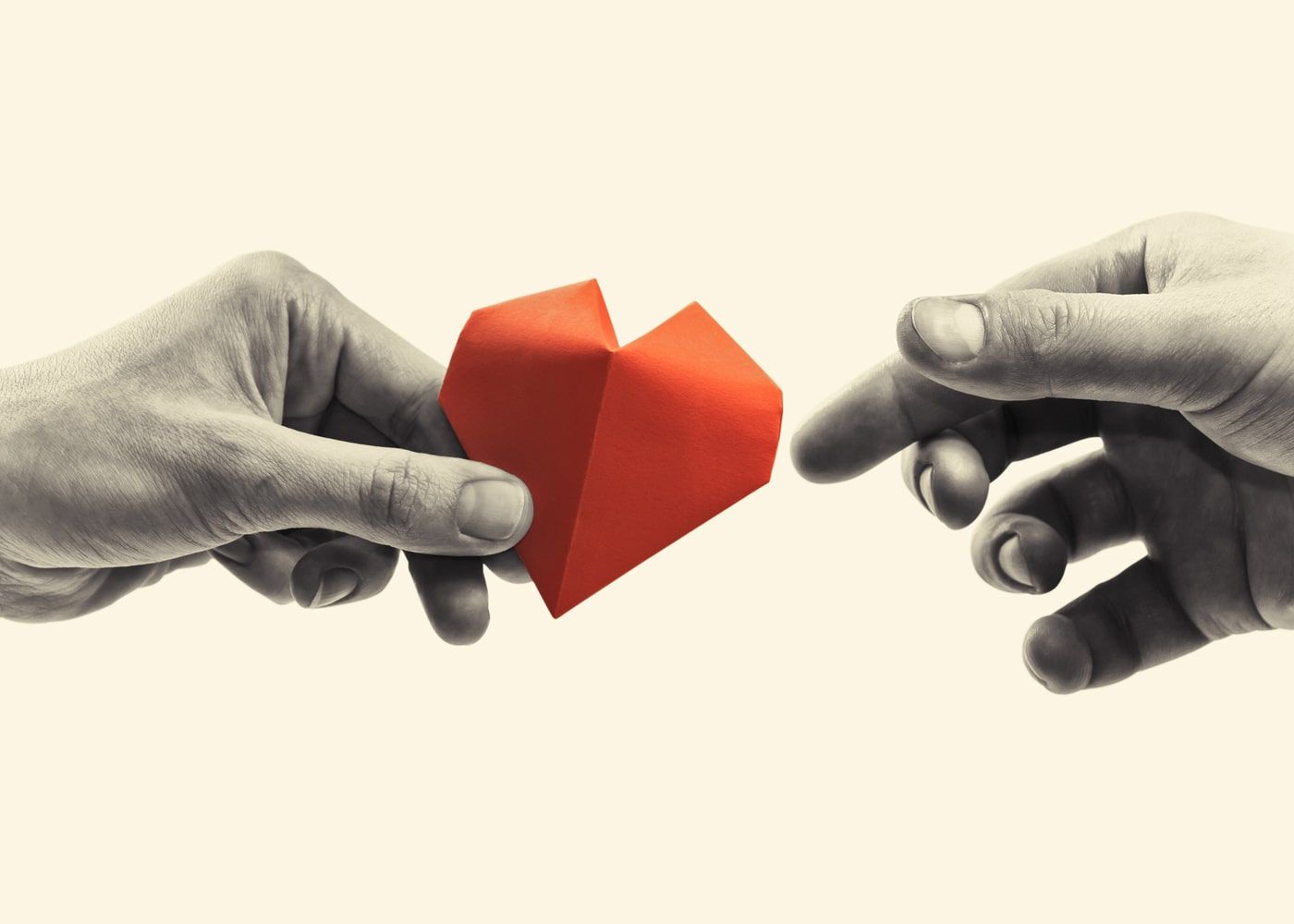 Two hands reaching toward a red origami heart on a light background
