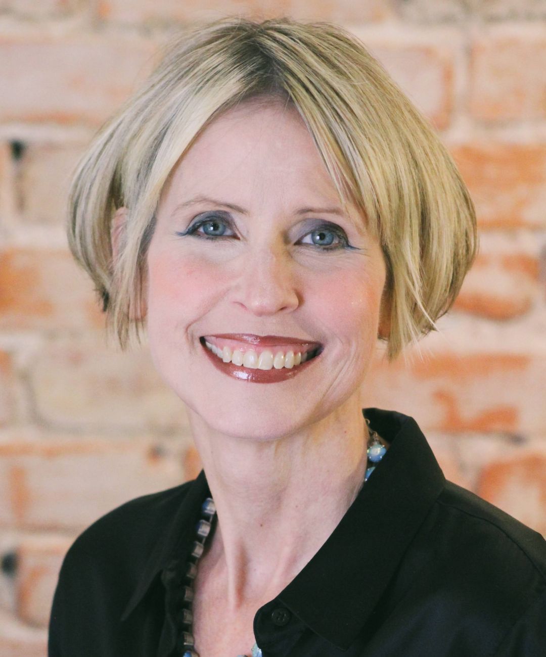Smiling blonde woman in a black shirt against a brick wall background